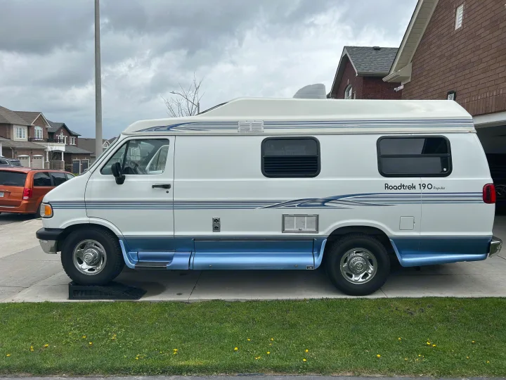 White & blue Roadtrek 190 Popular RV camper van, ready for your rv rental. Parked on a driveway with cloudy skies.. Roadtrek 190 Popular 1997