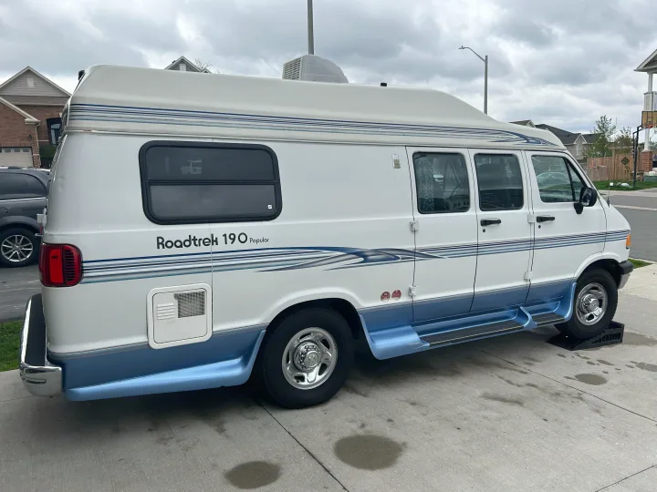 Discover this white and blue Roadtrek 190 camper van. A great rv rental option for travel adventures, parked on leveling ramps.. Roadtrek 190 Popular 1997