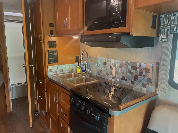 Compact kitchen in an RV rental, featuring a double sink, stove, microwave, and utility controls.. Winnebago Minnie Winnie 2019