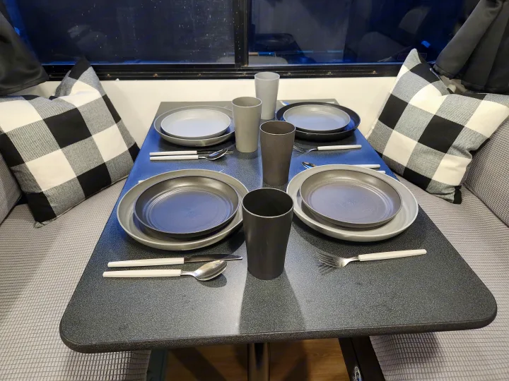 RV rental dining area with a table set for four: grey dishes, cups, white cutlery, and cozy checkered pillows.. Four Winds Majestic 2008