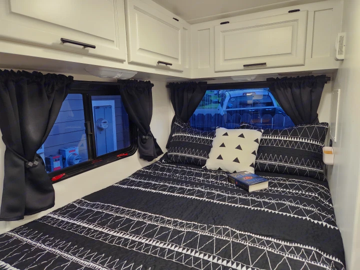 RV rental bedroom: a cozy space with a black & white bed, tie-back curtains on windows, and white overhead cabinets.. Four Winds Majestic 2008