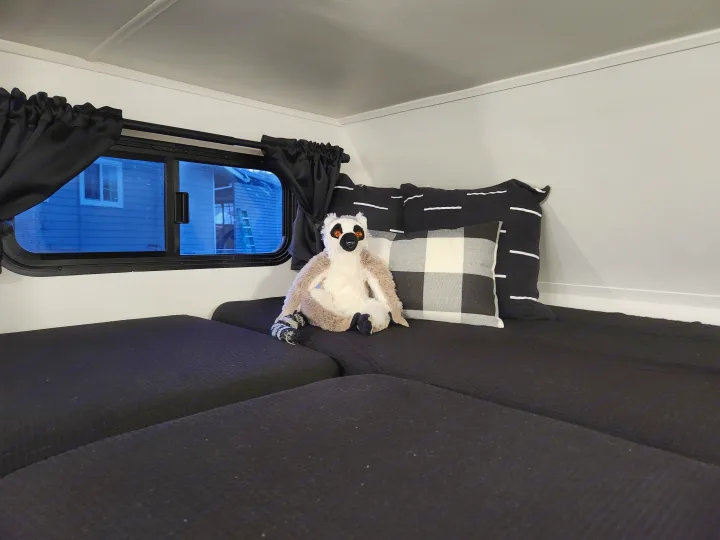 Cozy RV rental interior with a comfortable black bed, window, and a playful lemur plush.. Four Winds Majestic 2008