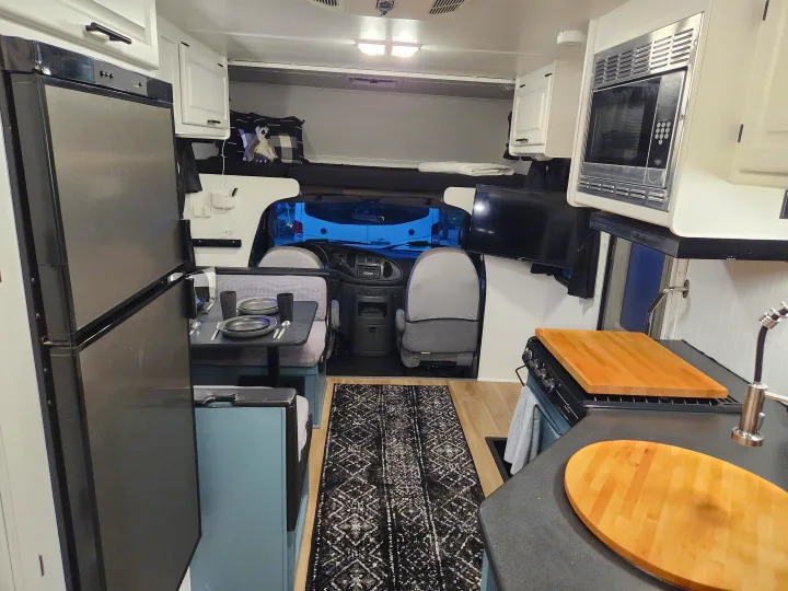 A well-appointed RV rental interior featuring a kitchen with fridge, microwave, stove, dining area, and cab-over bunk bed.. Four Winds Majestic 2008