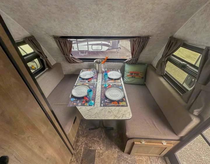 Bright RV rental interior showing a dining area with a set table for four, comfortable benches, and scenic windows.. Prolite Evasion 2021