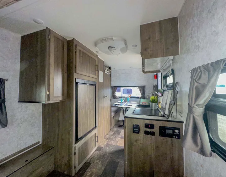 Cozy RV rental interior featuring a compact kitchen, dining area, refrigerator, and overhead cabinets, ideal for travel.. Prolite Evasion 2021