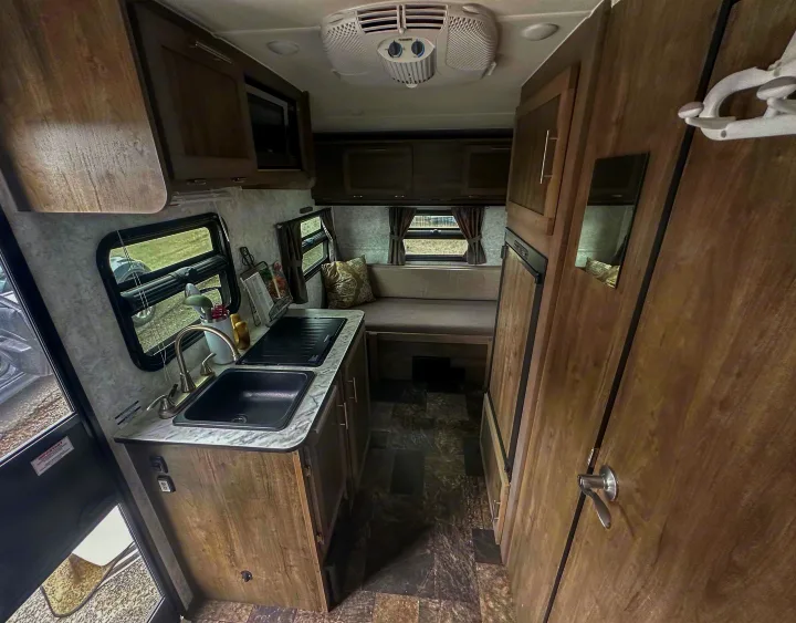 Inside this rv rental: a compact kitchen with sink, microwave, and dinette seating. Wood-look cabinetry and flooring.. Prolite Evasion 2021
