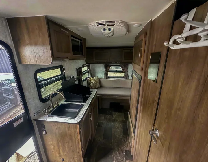 This RV rental interior features a compact kitchen with sink and stove, cozy dining area, and overhead storage, perfect for camper travel.. Prolite Evasion 2021