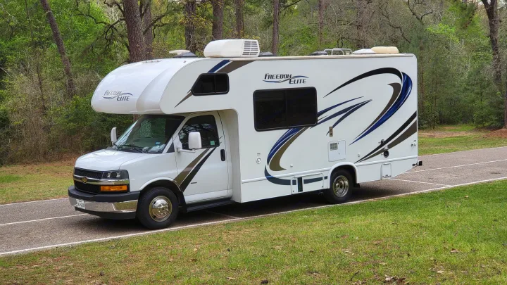White Class C RV rental, "Freedom Elite" model, parked on a paved path in a forest. This camper or motorhome is ready for adventure.. Thor 22HE 2019