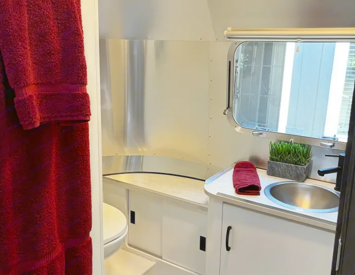 Modern rv rental bathroom with compact sink, black faucet, toilet, sleek aluminum walls, and a window view.. Airstream Caravel 2021
