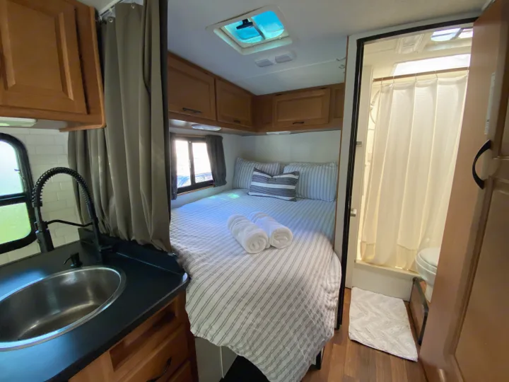 Cozy RV rental interior featuring a bed with fresh linens, compact kitchen, and bathroom. Perfect for travel adventures!. Thor Majestic 2015