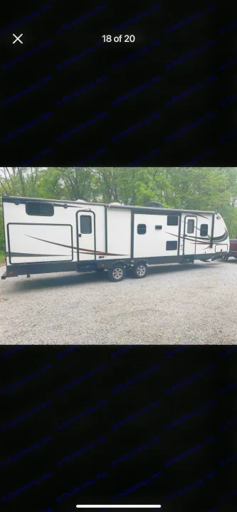 Side view of a long white & black travel trailer RV rental with slide-outs, parked on a gravel lot.. Heartland RVs Sundance XLT 2016