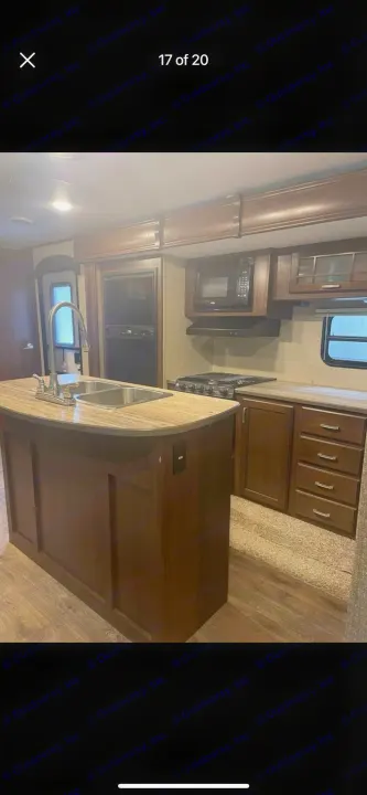 RV rental kitchen: island with sink, modern fridge, microwave, stove, and ample wood cabinets for storage. Ready for your journey.. Heartland RVs Sundance XLT 2016