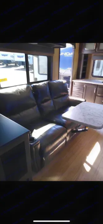 Bright rv rental interior: black reclining sofa, marble table, and kitchen area. Cozy, spacious, ready for adventure.. Grand Design Imagine 2018