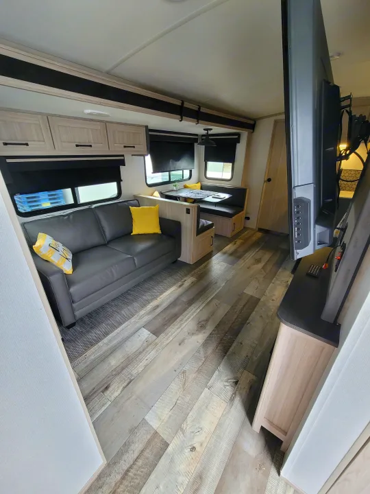 RV rental interior with a cozy sofa, dinette, and TV. Features modern light wood cabinets & plank flooring.. Heartland RVs Sundance Ultra Lite 2022
