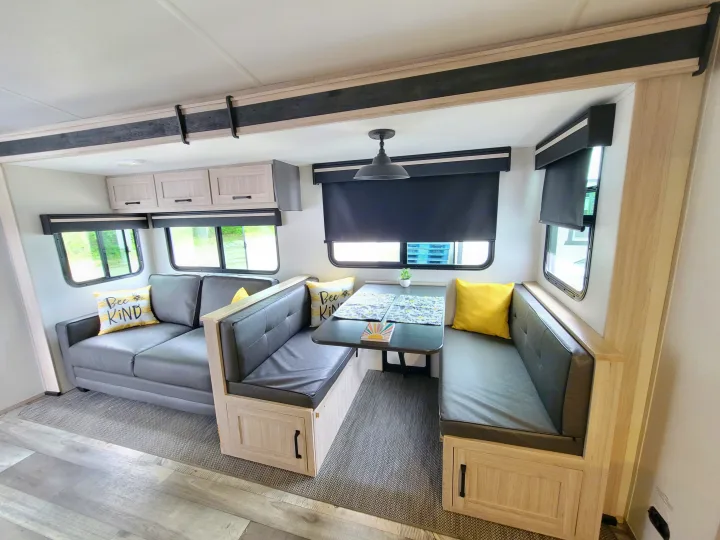 Bright RV rental interior with a gray sofa and U-shaped dinette in light wood, featuring modern dark accents.. Heartland RVs Sundance Ultra Lite 2022