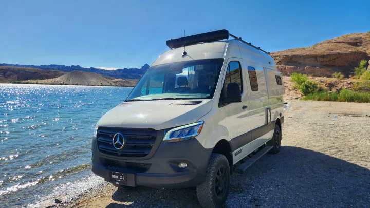 Scenic RV rental adventure: A white Winnebago Revel camper van by a shimmering lake with mountains in the background.. Winnebago Revel 2022