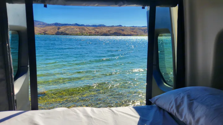 Panoramic lake & mountain views from an RV rental. Cozy bed & sparkling clear water just outside. Perfect travel camping!. Winnebago Revel 2022