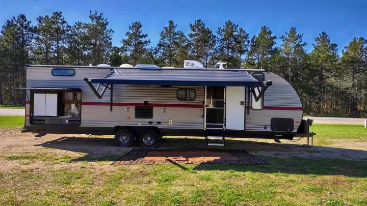 An RV rental, a Grey Wolf travel trailer, is set up for camping with an outdoor kitchen, awning, and mat.. Forest River Cherokee Grey Wolf 2019