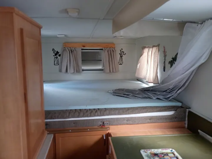 Inside an RV rental: a bright, comfortable sleeping area with a foam mattress, draped windows, and practical cabinetry.. Trailmanor Trailmanor Trailer 2005