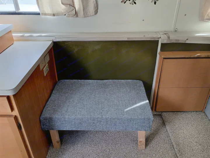 Inside an rv rental, a compact living space with a grey bench, light counter, and wood cabinets. Perfect for travelers.. Trailmanor Trailmanor Trailer 2005