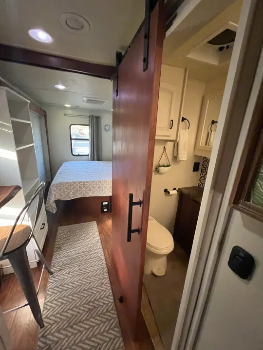 Cozy bedroom with barn door to compact bathroom inside an rv rental, showcasing efficient mobile living.. Jayco Seneca 2013