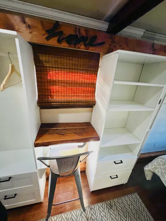 Compact RV rental workspace with built-in desk, storage, shelving, and drawers, featuring a cozy 'home' sign and industrial stool.. Jayco Seneca 2013