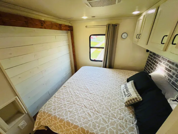 Cozy rv rental bedroom showing a bed, shiplap wall, window, and brick-patterned headboard.. Jayco Seneca 2013