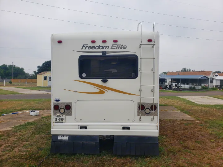 Rear view of a white Freedom Elite RV rental with a ladder and Texas plate, parked in a grassy RV park.. Four Winds Freedom Elite 2010