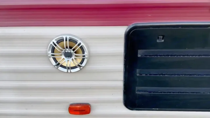 Part of an RV rental's exterior, showing a speaker, black utility vent, and red marker light on the corrugated siding.. Forest River Cherokee Grey Wolf 2019