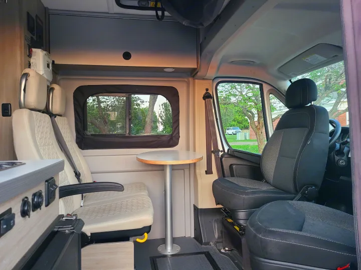 RV rental interior with comfortable passenger seats, dining table, and utility controls. Also shows front cabin for travel.. Winnebago Solis 2021
