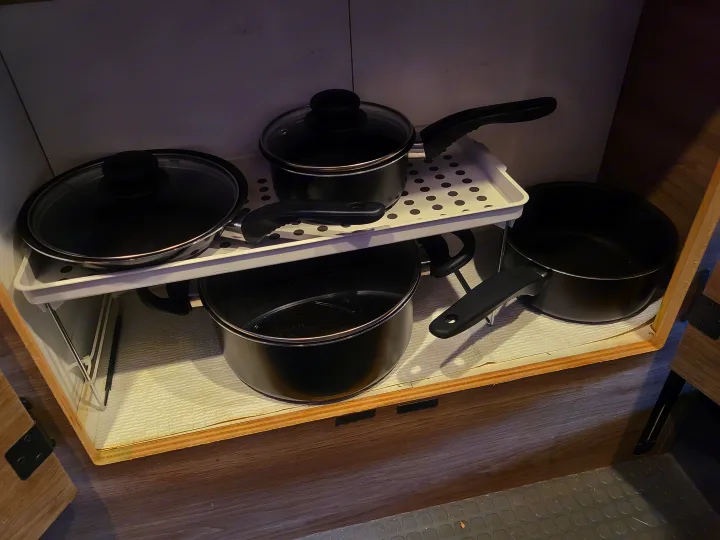 Efficient kitchenware organization in an RV rental: black pots and pans are neatly stored on a multi-level shelf inside a cabinet.. Winnebago Solis 2021