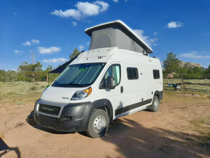 White pop-top camper van parked on a dirt road. Perfect for your next rv rental adventure under a clear blue sky.. Winnebago Solis 2021