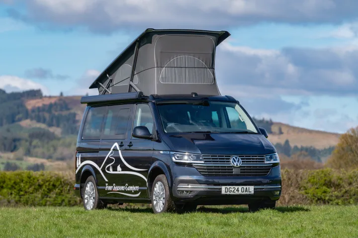 Dark blue Volkswagen California campervan, pop-top extended, in a grassy field. Perfect for your Four Seasons Campers RV rental adventure.. Volkswagen California Ocean 2024