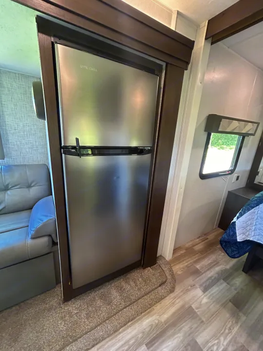 RV rental interior features a stainless steel refrigerator, a gray sofa in the living area, and a bedroom beyond.. Forest River Salem 2020
