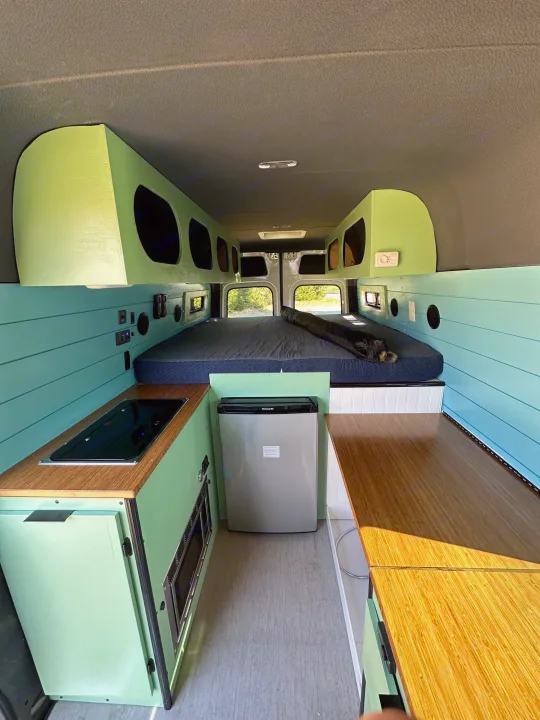 Modern RV rental interior, featuring a bright green and blue kitchen, sleeping area, and storage.. Mercedes-Benz Sprinter 2021