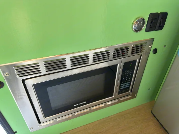 Greystone microwave, water gauge, and switches on a green panel, showcasing an RV rental interior's amenities.. Mercedes-Benz Sprinter 2021