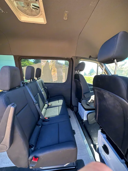 Inside a spacious RV rental: multi-row black seating, light flooring, and a ceiling fan.. Mercedes-Benz Sprinter 2021