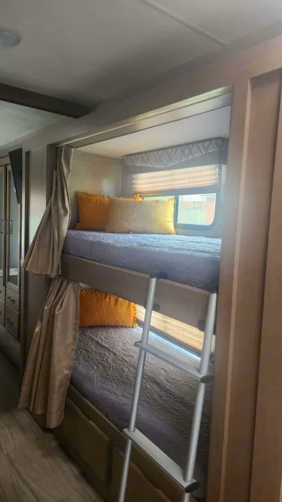 This RV rental features comfy bunk beds with yellow pillows, a ladder, and window blinds, offering a cozy sleeping space.. Thor Quantum 2021