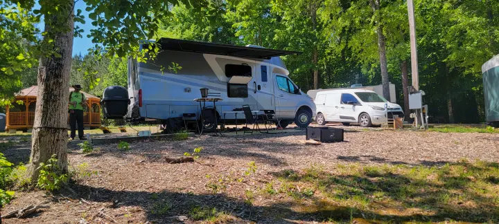 RV rental setup at a shady campground, complete with grill, awning, and outdoor seating for a comfortable outdoor living experience.. Wayfarer Wayfarer Motorhome 2024