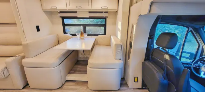 RV rental interior: a bright, modern dining area with table, two benches, additional seating, and a glimpse of the cockpit.. Wayfarer Wayfarer Motorhome 2024
