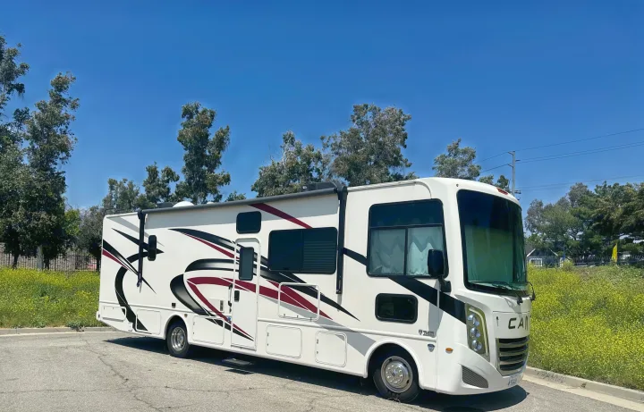 Spacious white RV rental parked on a sunny day, set against a backdrop of green trees and yellow flowers.. Thor A.C.E. 2023