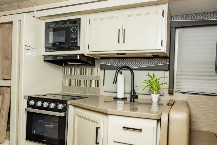 This RV rental features a modern kitchen with a microwave, oven, sink, and stylish backsplash, plus ample storage.. Thor A.C.E. 2023