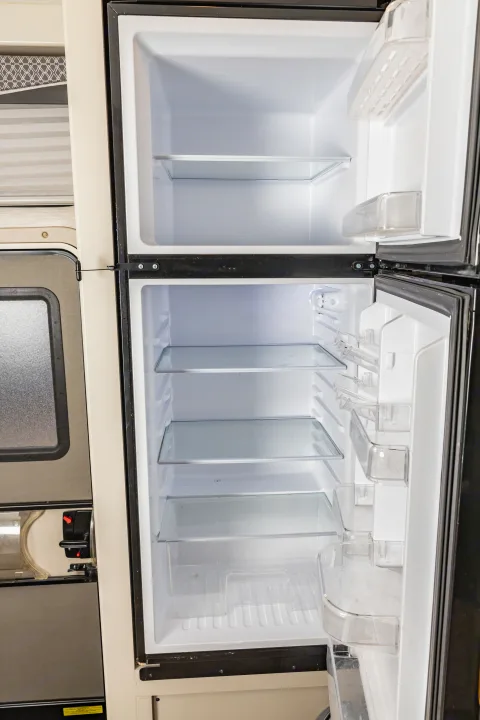 Empty two-door RV rental fridge and freezer, with clean shelves and clear door bins.. Thor A.C.E. 2023