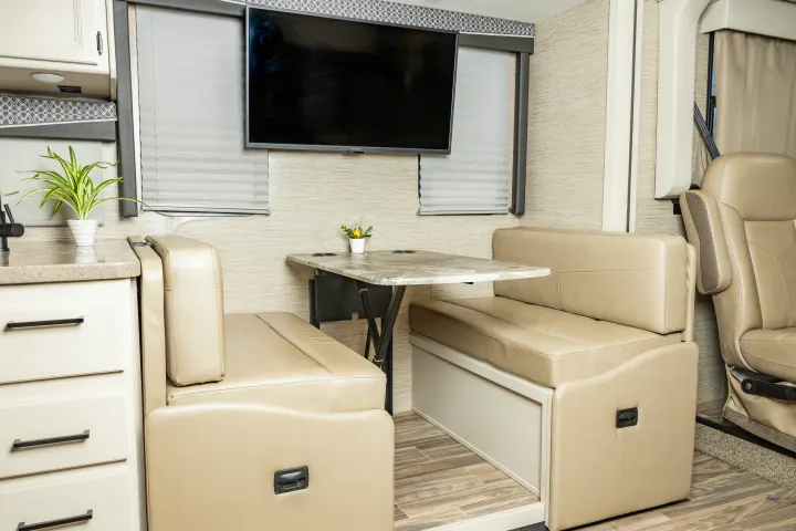 This inviting RV rental interior showcases a cozy dinette, wall-mounted TV, and functional kitchen area.. Thor A.C.E. 2023