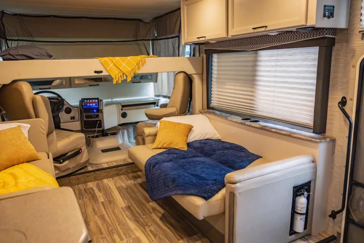 Inside a modern rv rental: bunk bed, driver's cockpit, and convertible sofa with window blinds.. Thor A.C.E. 2023