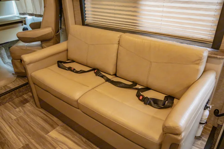 RV rental interior: A beige sofa with black seatbelts, showing travel-ready passenger seating in a motorhome.. Thor A.C.E. 2023