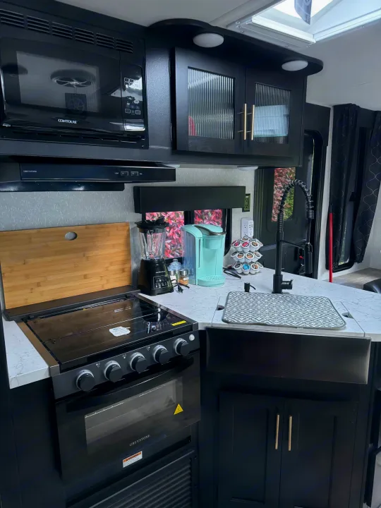 Modern RV rental kitchen: black microwave, stove, sink, and light gray counters. Sleek design for travel comfort.. Greywolf 23MK 2022