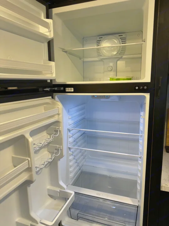 Inside an empty RV rental refrigerator, a two-door unit with top freezer and bottom fridge, featuring shelves, ready for your trip.. Greywolf 23MK 2022