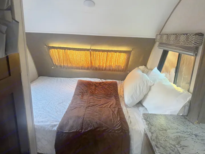 Cozy RV rental bedroom with bed, sunlit windows, curtains, hanging storage, and a small counter area.. R-Pod R-Pod Trailer 2018