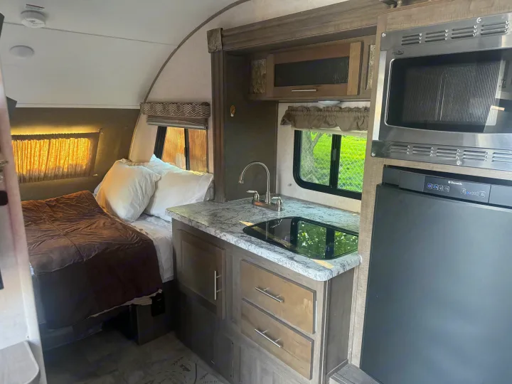 Cozy RV rental interior features a compact kitchen with microwave, sink, cooktop, and refrigerator, plus a comfortable bed.. R-Pod R-Pod Trailer 2018